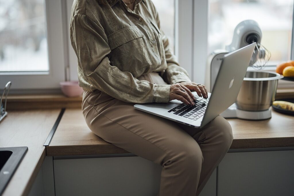 Woman using a laptop at home in a kitchen setting, representing virtual or remote access to services.