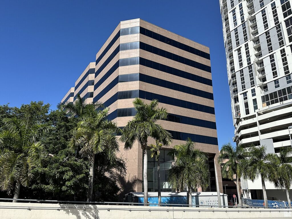 Exterior of the City of Miami Office Building with palm trees and a neighboring high-rise under construction.