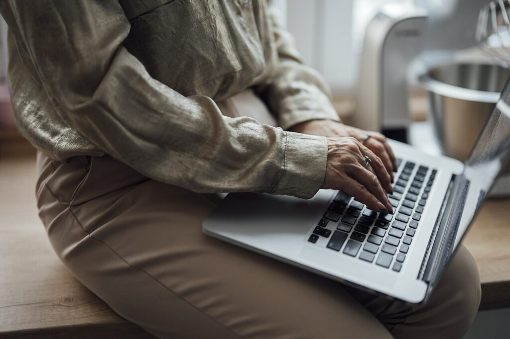 Woman using a laptop while sitting on a kitchen counter.