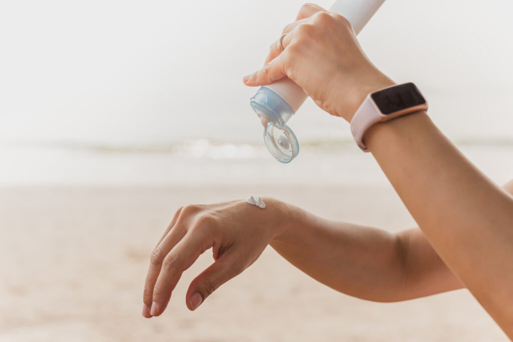 Person dispensing sunscreen onto the back of a hand at the beach.